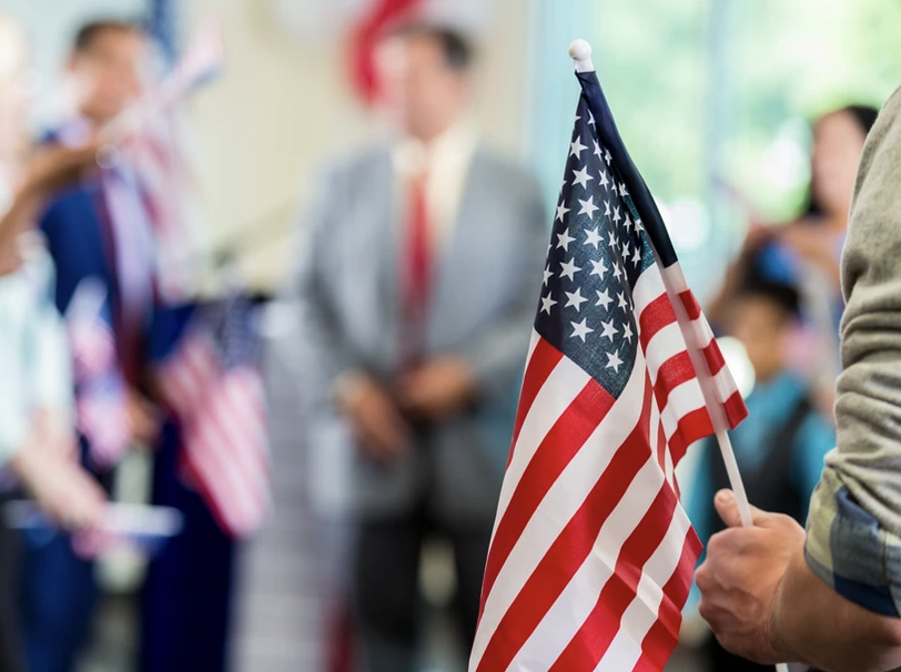 Image of a U.S. flag being held by a white hand with a blurred background